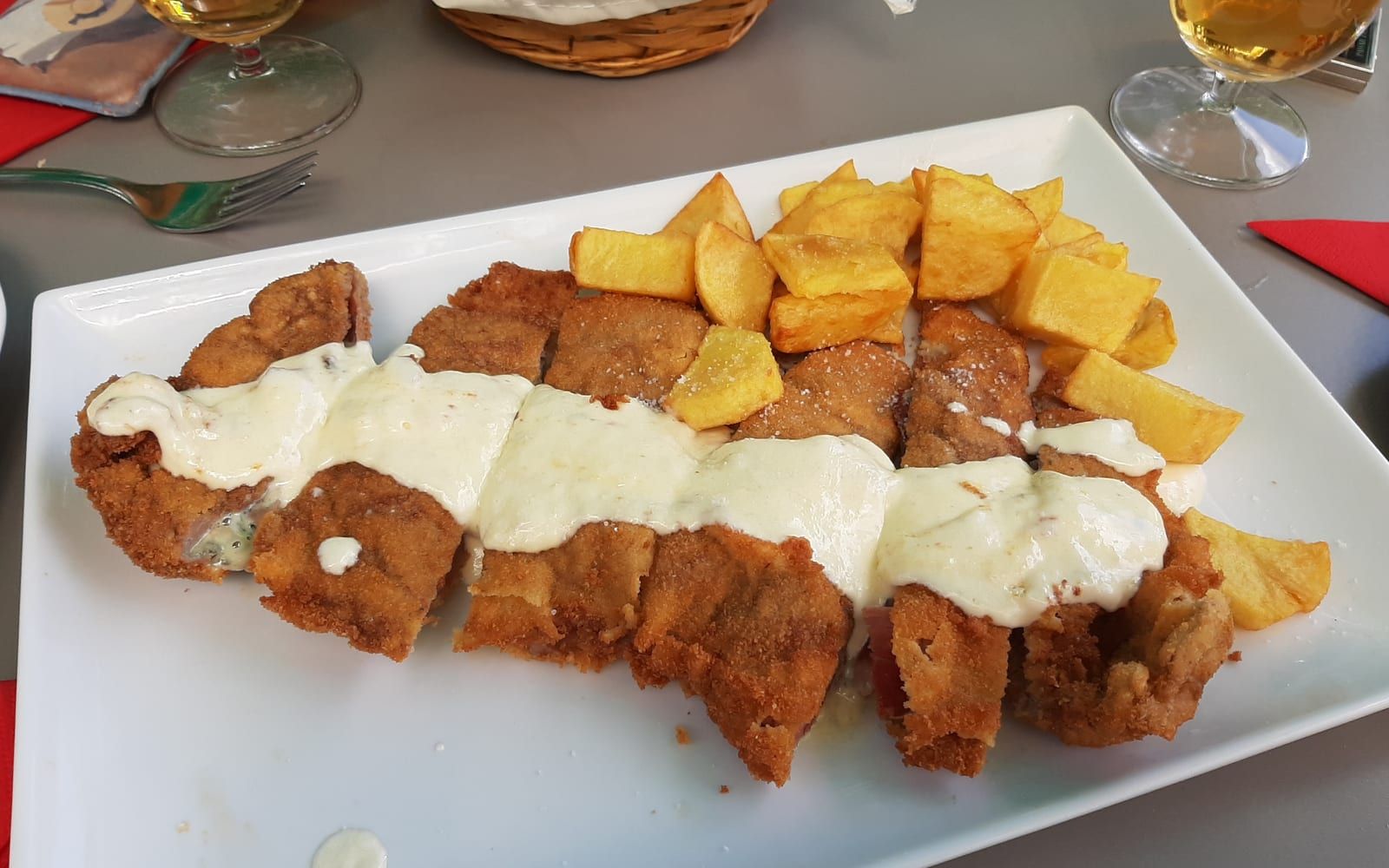 Filete empanado relleno, cortado en tacos, con salsa de queso y patatas fritas
