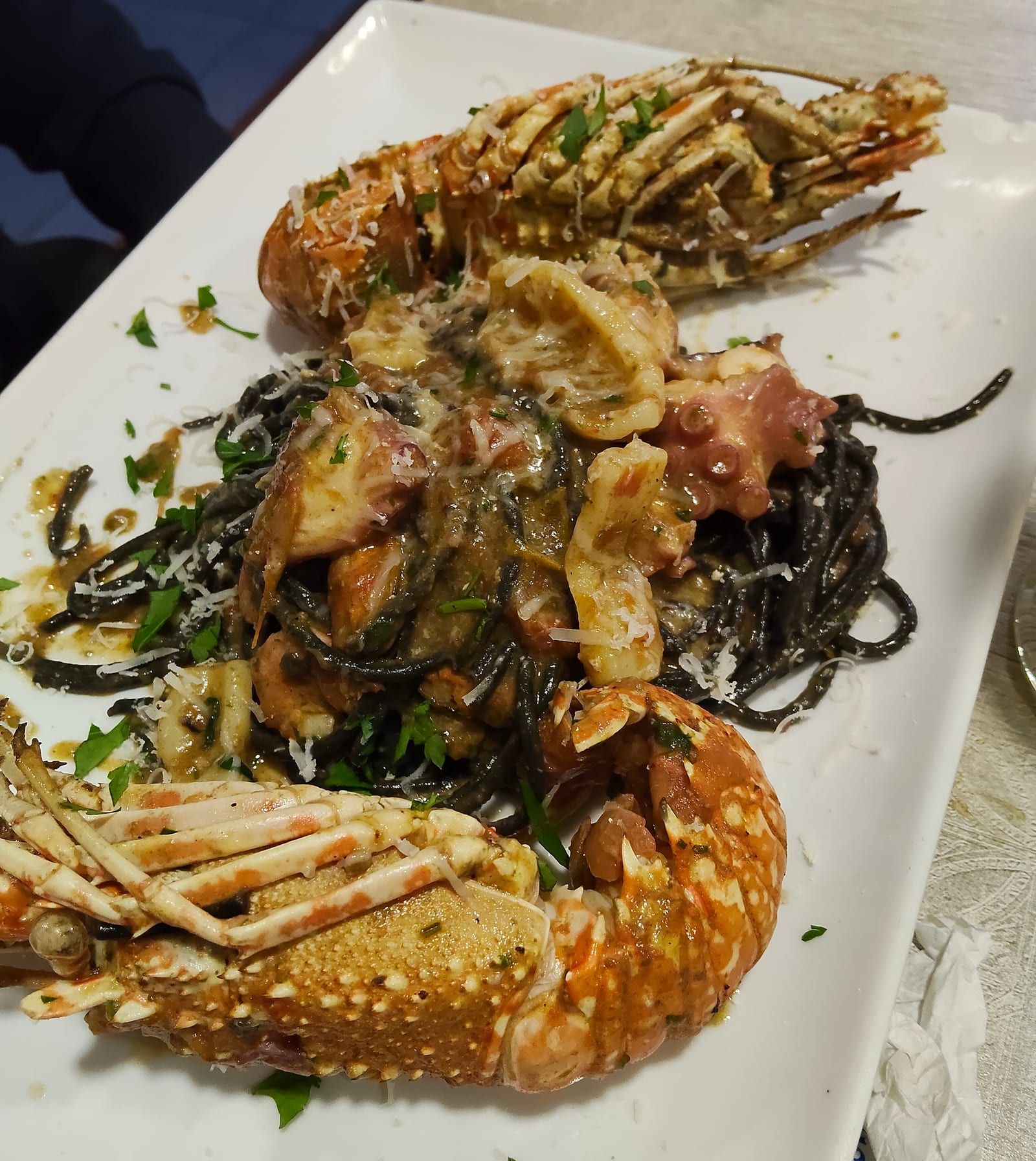 Espaguetis negros con langosta, calamar y pulpo en fuente blanca