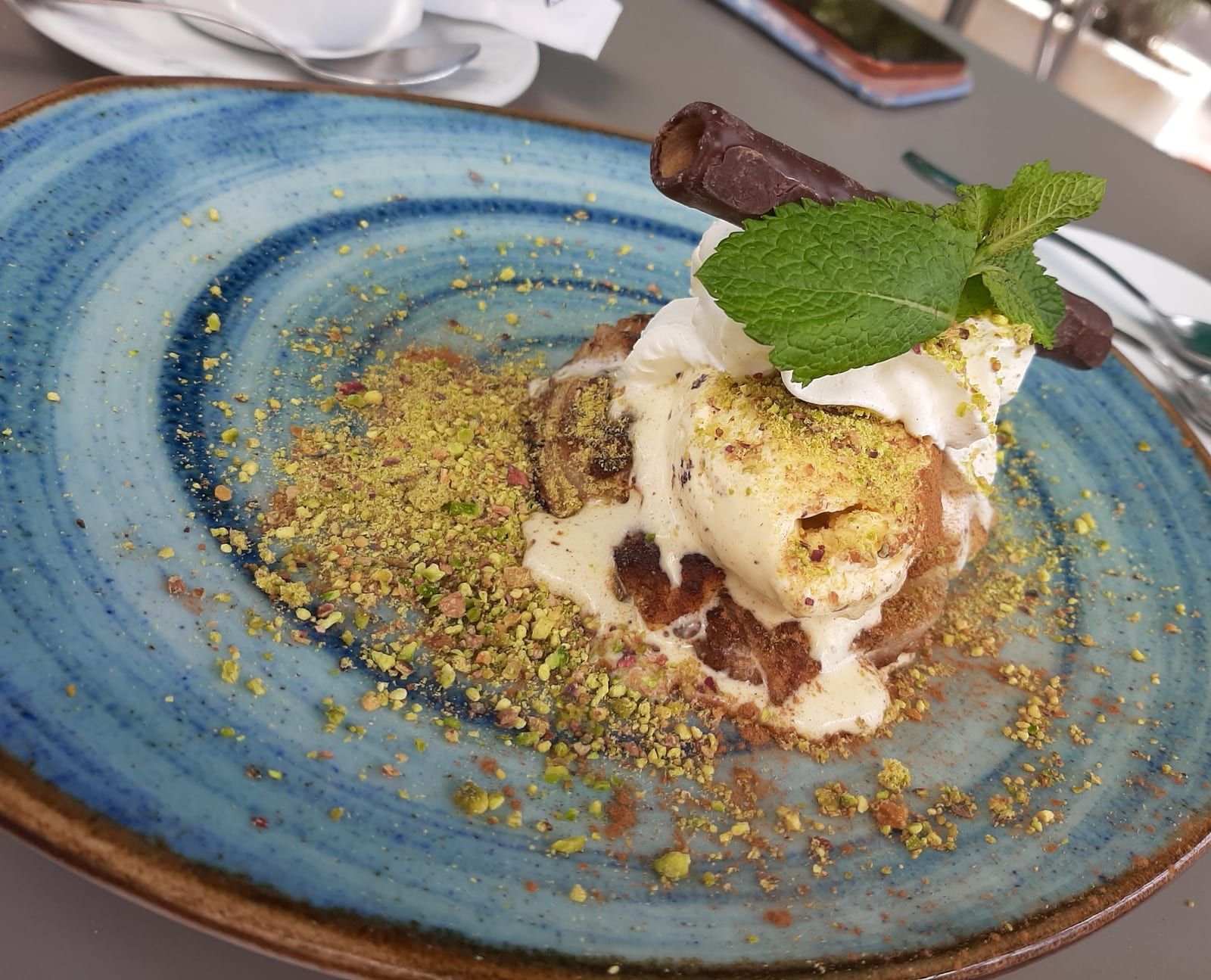 Postre con helado, nata y pistacho picado sobre un plato de cerámica azul
