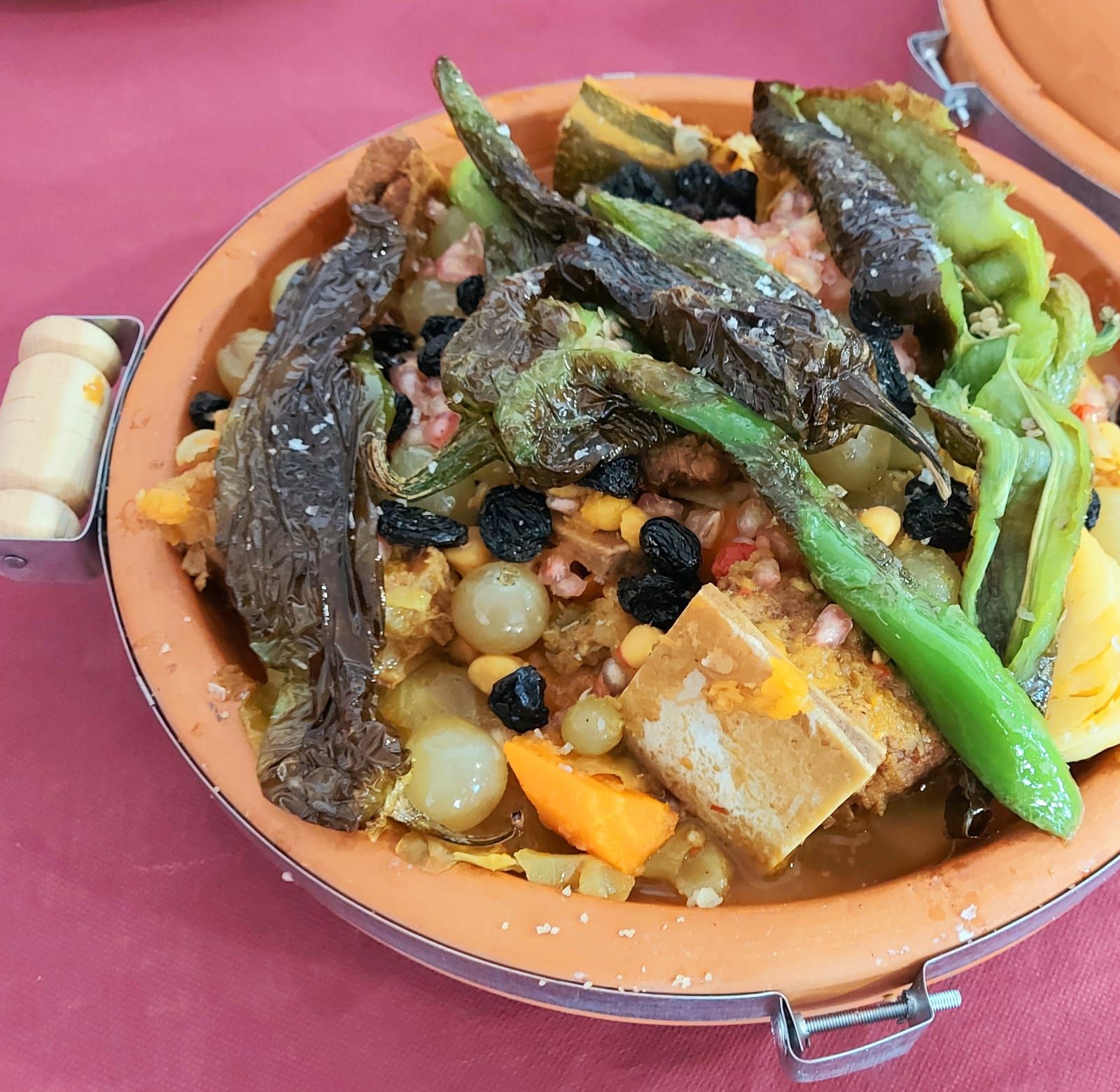 Tayín servido en su cazuela de barro, con verduras, pasas y pimientos asados