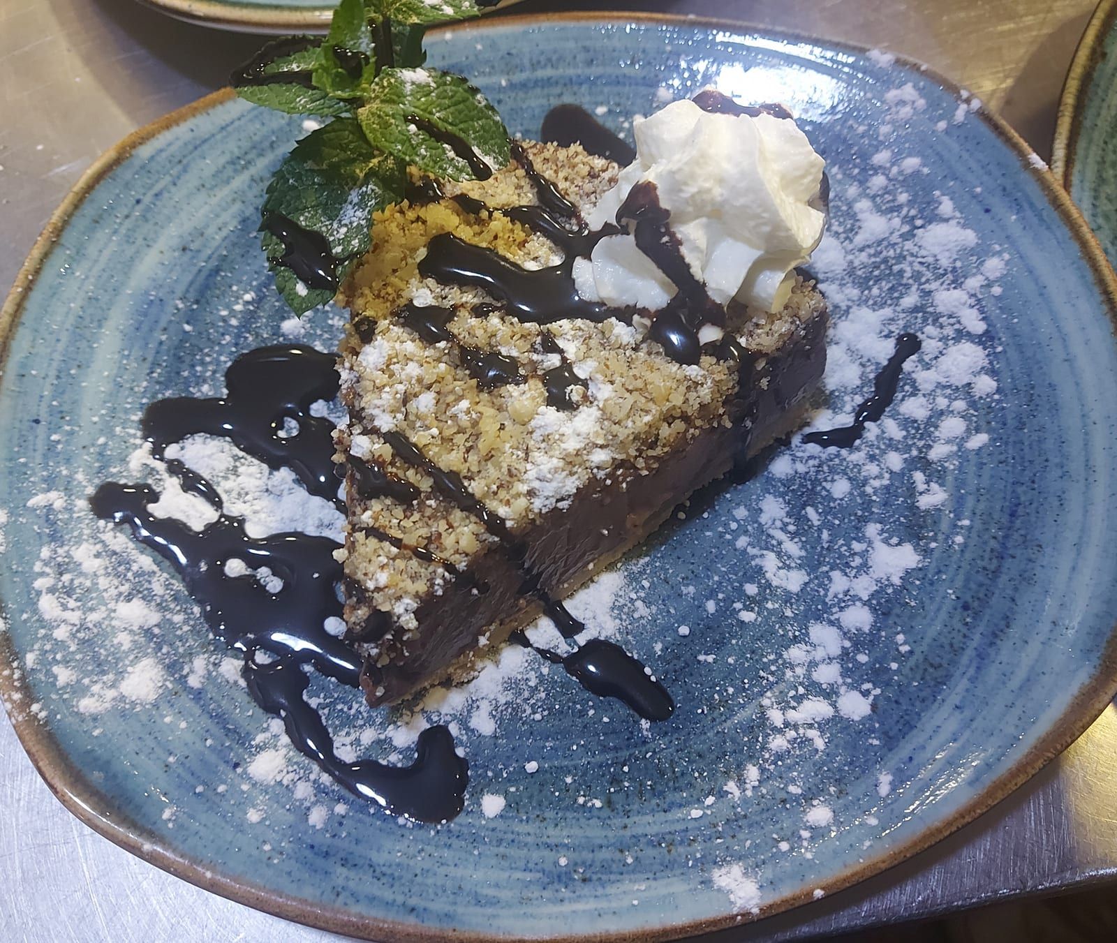 Porción de tarta de chocolate con almendra picada, nata y hierbabuena